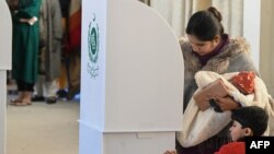 په اسلام اباد کې یوې ښځې بچی په غېږ کې نیولی او ووټ اچوي، څنګ کې یې بل ماشوم هم ولاړ دی - د فبرورۍ اتمې انځور.