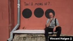 Hamlet Zinkivskiy sits in front of a mural he created in Kharkiv. The wording reads: "Yes! Or maybe no?"