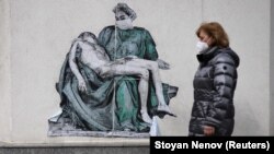 A woman walks past a mural depicting a medical worker in a pose like that of Michelangelo's famous Pieta sculpture, on a wall near a vaccination center in the Bulgarian capital, Sofia.