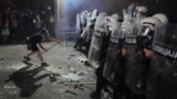 Демонстрант со гас-маска ги удира штитовите на полицајците во кордонот во Нови Сад. 5 септември 2025 година