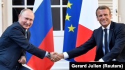 French President Emmanuel Macron (right) shakes hands with Russian President Vladimir Putin at his summer retreat on the Mediterranean coast on August 19.